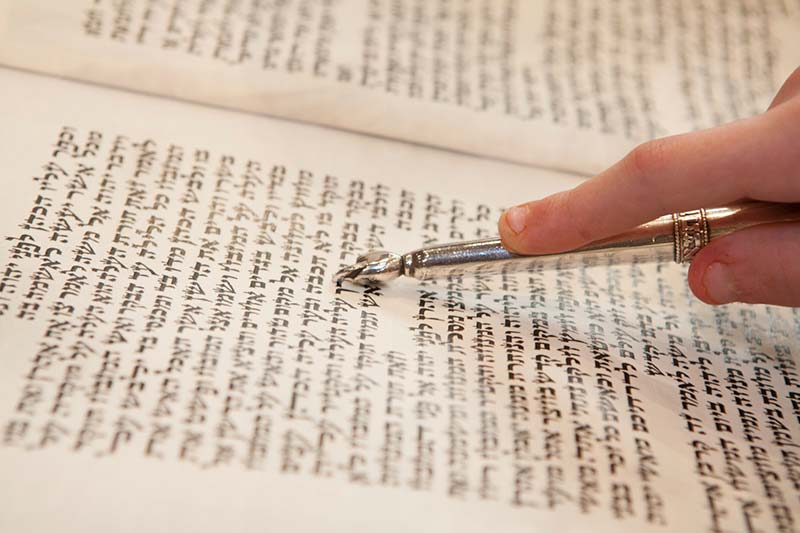 Child holding a yad, or silver pointer, over Hebrew text.