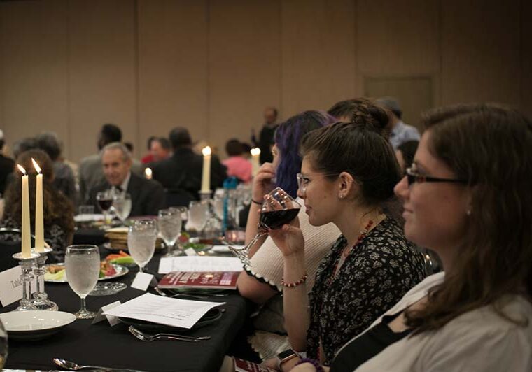 Young women enjoying shabbat meal near burning candles. One of them is drinking wine.