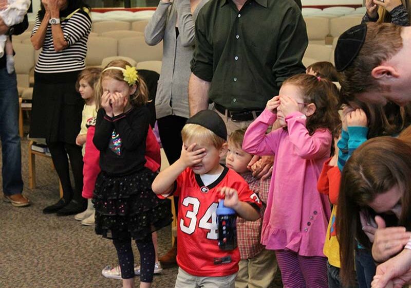 Children saying the Sh'mah prayer with their eyes closed during Tot Shabbat in the Sanctuary